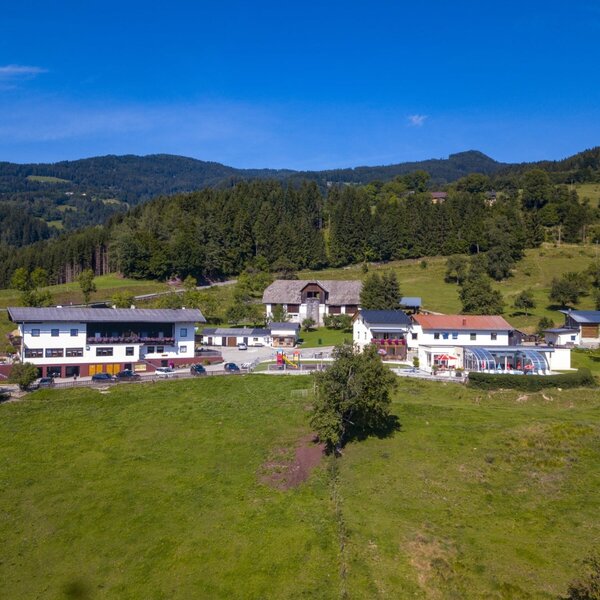 The Ap­par­te­ments with an outdoor pool, playground, and parking, surrounded by green meadows and forests.