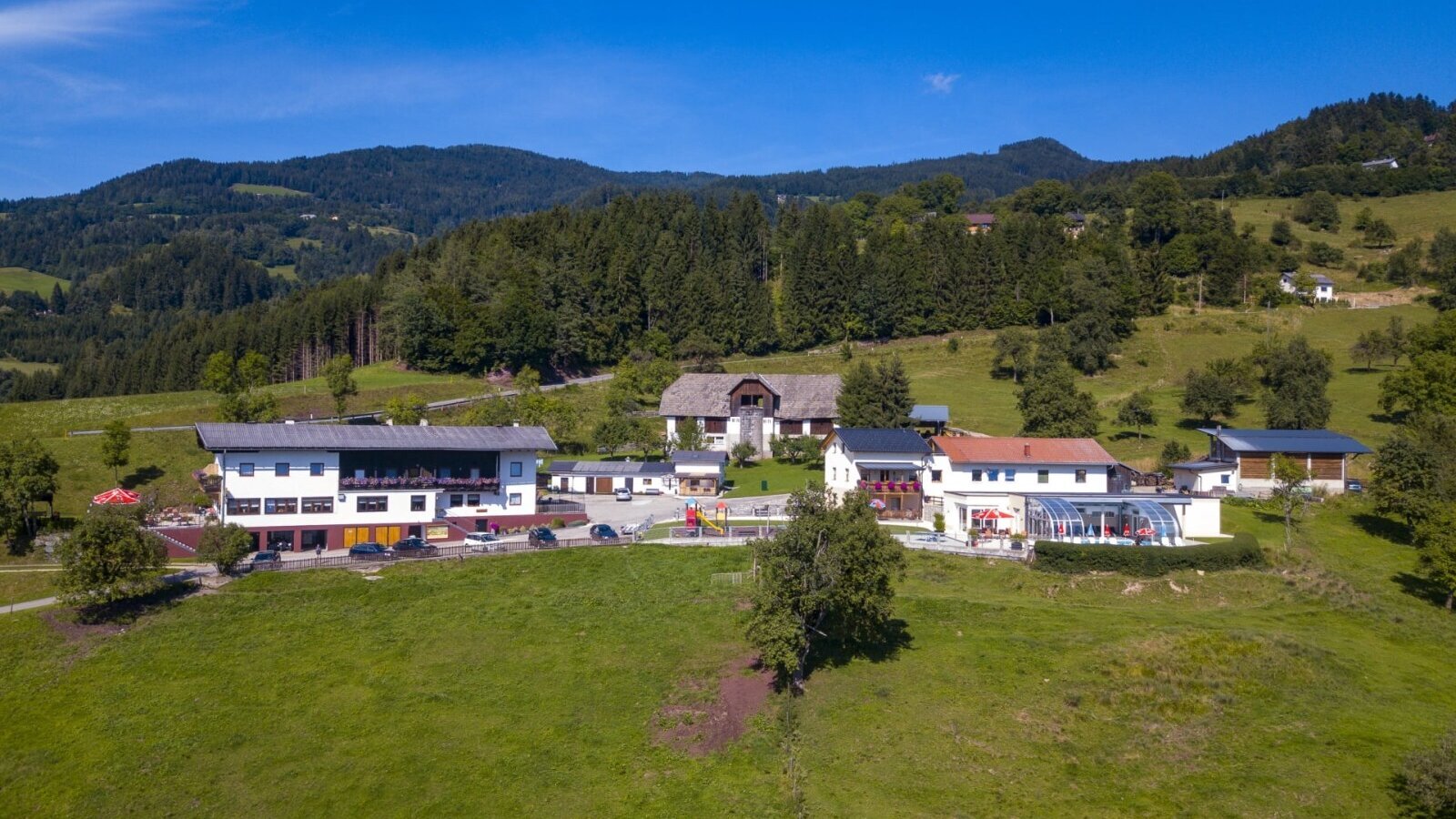 The Ap­par­te­ments with an outdoor pool, playground, and parking, surrounded by green meadows and forests.
