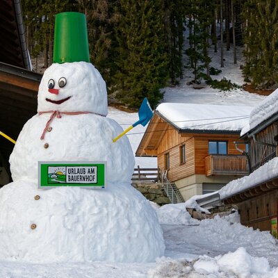 A large snowman with a "Holiday on the Farm" sign stands outside the Farm House, surrounded by snow.