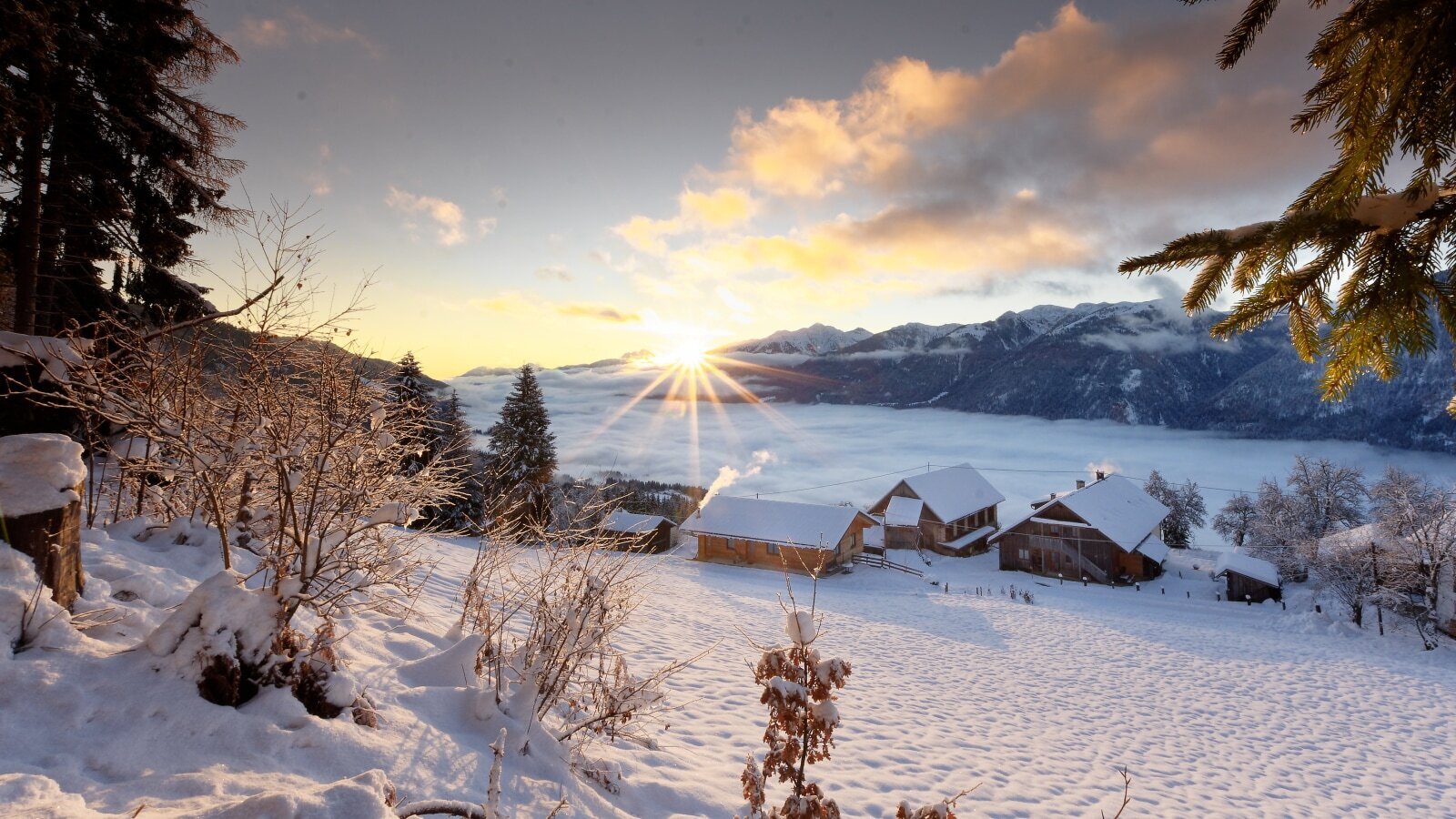 The Farm House buildings set against a snowy mountain backdrop, overlooking a misty valley during sunrise.