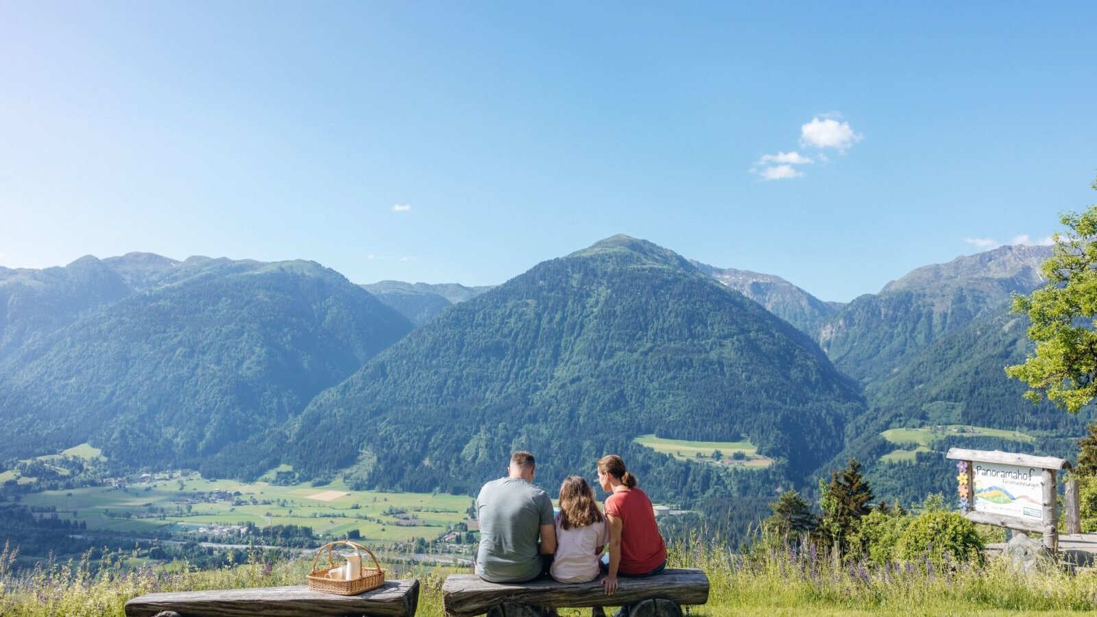 Expansive mountain view from the Bauernhof, enjoyed by a family on a wooden bench with a picnic basket.