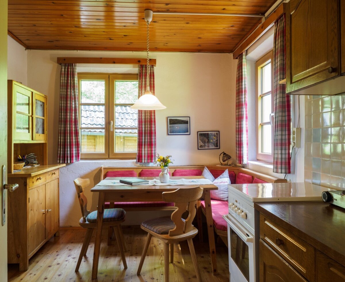 Dining area with a wooden table, corner bench, and an integrated kitchen featuring a stove in this Alpine Hut.