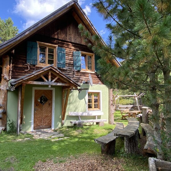The exterior of the Alpine Hut, featuring a wooden facade, green shutters, and an outdoor seating area with carved wooden benches.