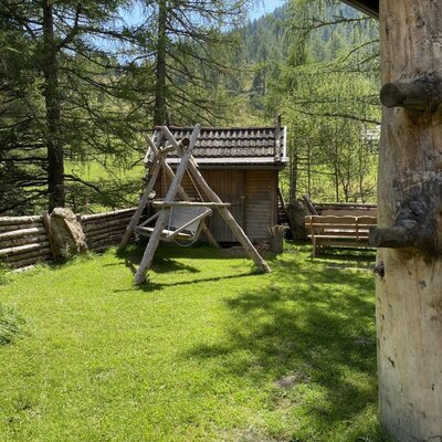 The Alpine Hut features an outdoor area with a wooden swing, a bench, and natural surroundings with trees and mountains.