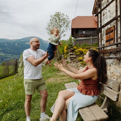 The outdoor green space at the farmhouse, featuring a wooden bench, scenic mountain views, and traditional architecture.