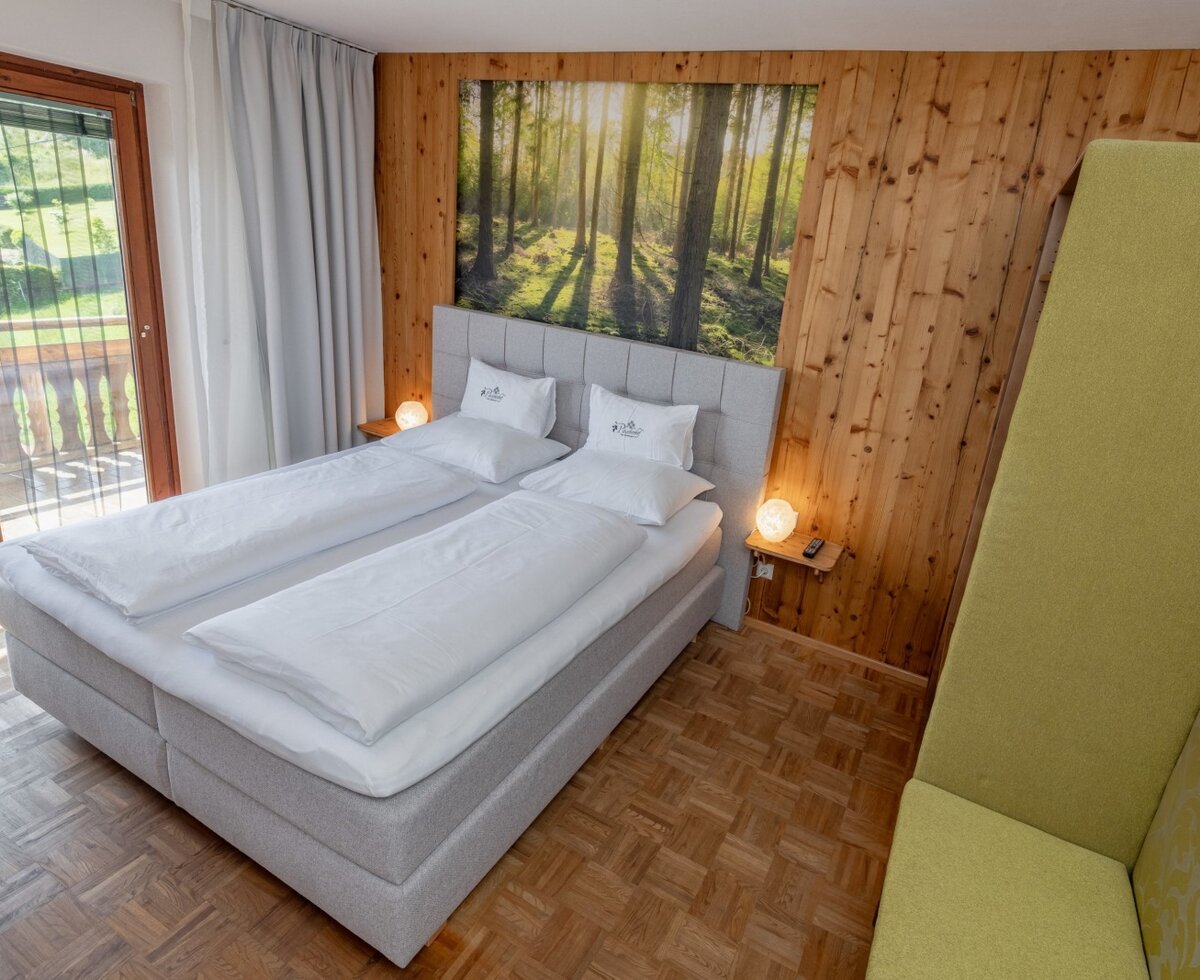 Double bedroom in the Farm House featuring a forest-themed wall art, wooden paneling, a seating area, and access to a balcony overlooking the green landscape.