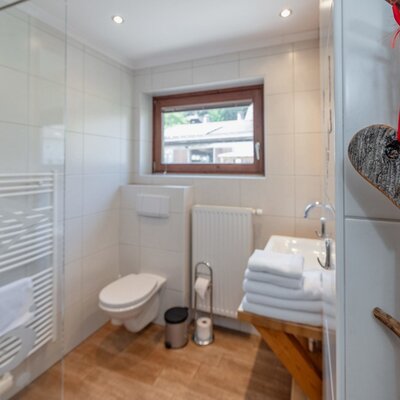 Farm House bathroom featuring a wall-mounted toilet, a sink with fresh towels, a shower area, a heated towel rail, and a window.