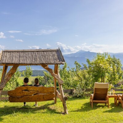 Outdoor seating area at the farmhouse featuring a wooden swing, two lounge chairs, and mountain views.