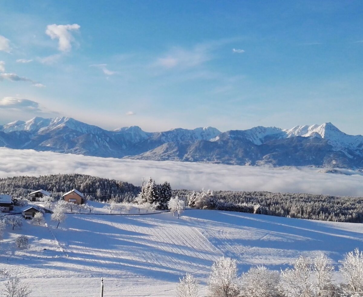 The Farm House is nestled among snow-covered fields and forests, offering views of distant mountains rising above a cloud-filled valley.