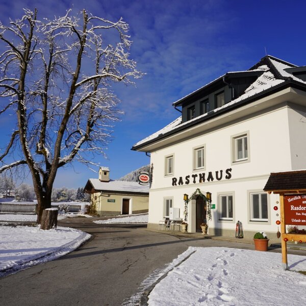 The Farm House exterior in winter, showing the white building labeled "Rasthaus" and a welcome sign for Rasdorferhof. The Farm House exterior in winter, showing the white building labeled "Rasthaus" and a welcome sign for Rasdorferhof.