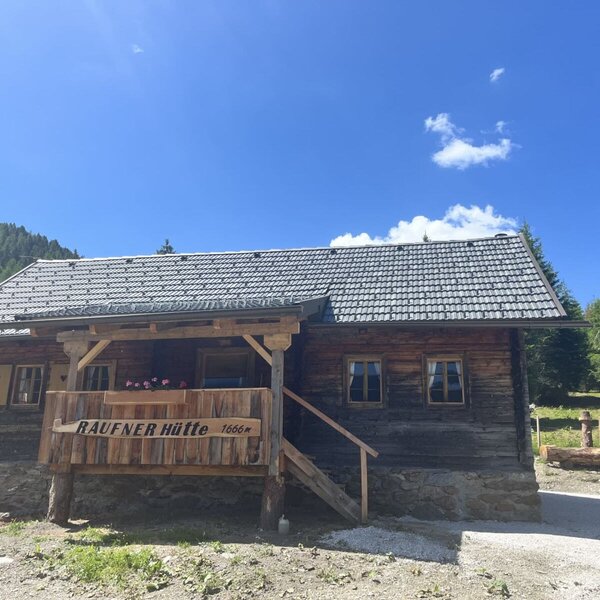 A rustic Alm set at 1,666 meters altitude, featuring a cozy wooden terrace under a bright blue sky.