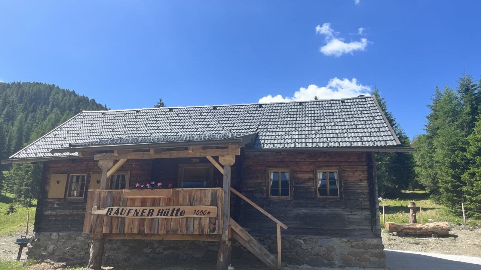 A rustic Alm set at 1,666 meters altitude, featuring a cozy wooden terrace under a bright blue sky.