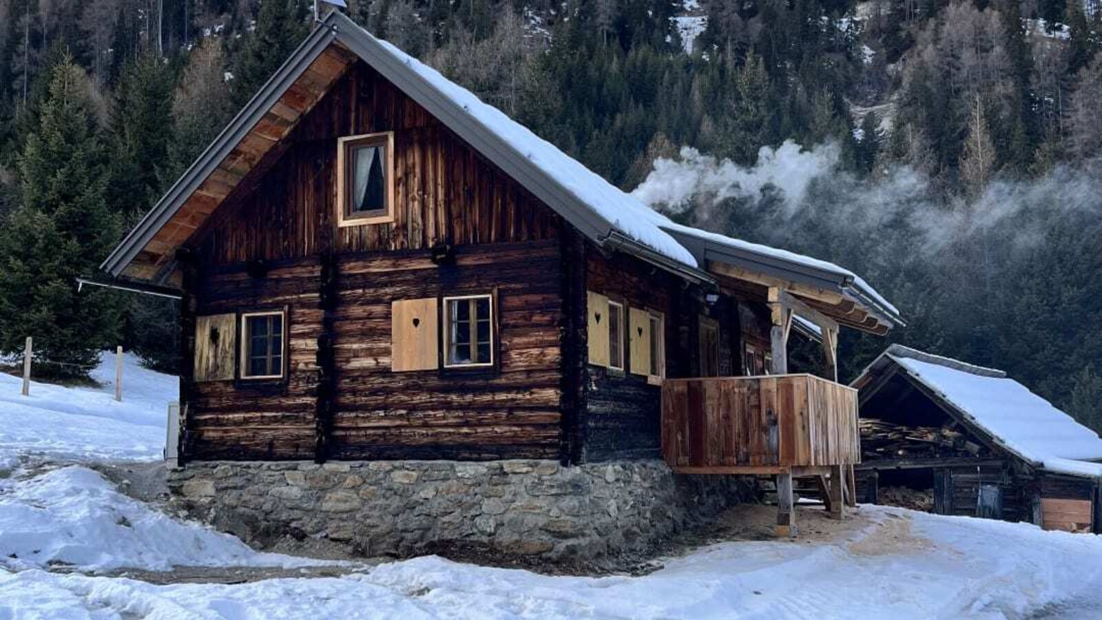 A rustic Alm in a snowy mountain landscape featuring a cozy wooden balcony against a wooded hillside.