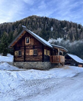 A rustic Alm in a snowy mountain landscape featuring a cozy wooden balcony against a wooded hillside.