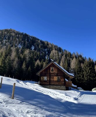 A rustic Alm set in a snowy winter landscape under a clear blue sky.
