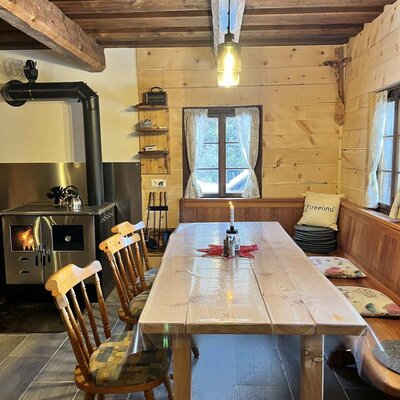 The Alm's cozy dining area featuring a rustic wooden table, comfortable bench seating, and a warm wood-burning stove.
