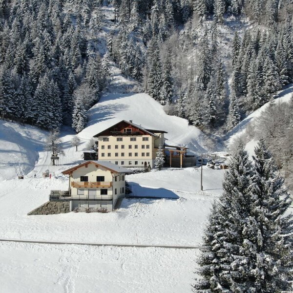 The farmhouse in a snowy mountain landscape with pine trees and ski slopes.