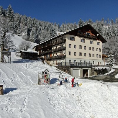 The farmhouse in winter, surrounded by snow and forest, with a children's playground.