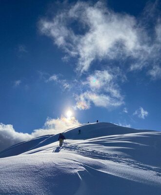 Ski tourers ascending a snowy mountain under a blue sky with clouds.