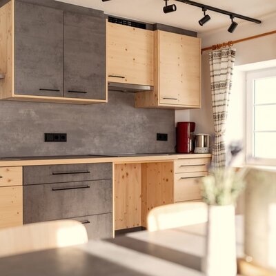 The modern kitchen in the farmhouse is equipped with wooden and grey cabinets, a sink, stovetop, coffee machine, and a window.