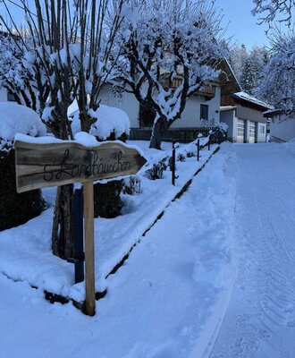 The snowy entrance to the holiday home, featuring a charming wooden sign and snow-covered trees.