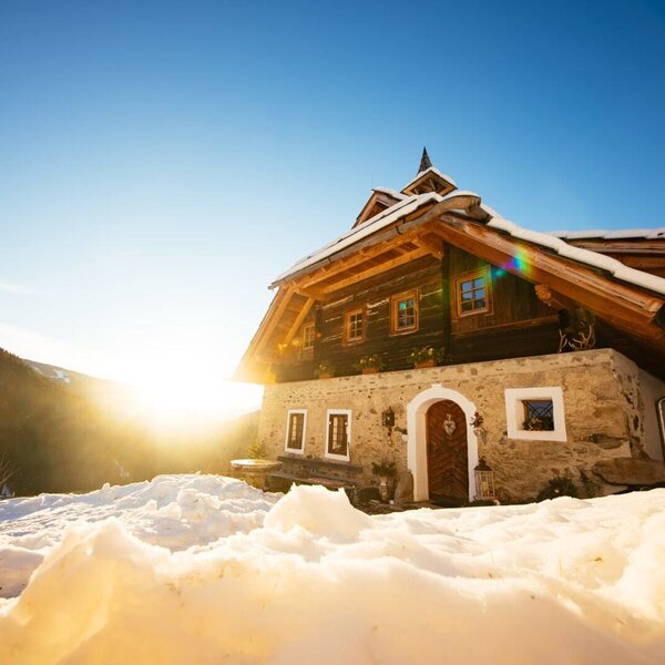The Alpine Hut's traditional exterior, built with a stone foundation and wooden upper levels, is surrounded by snow under a clear, sunny sky. The Alpine Hut's traditional exterior, built with a stone foundation and wooden upper levels, is surrounded by snow under a clear, sunny sky.
