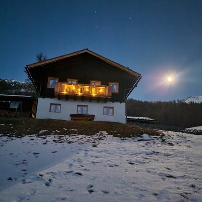 The Alm in the snow at night, with a lit balcony and a full moon.
