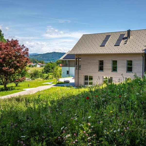 Exterior view of the Ferienwohnung with a wooden facade, surrounded by a blooming meadow and an access path.