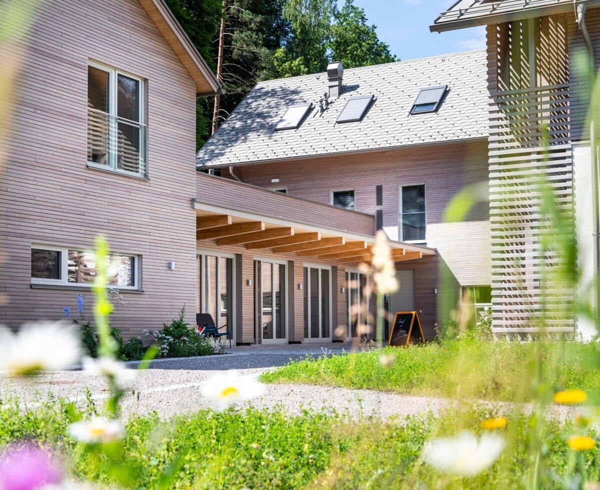 Exterior view of the Ferienwohnung with modern wooden facade and covered entrance area, surrounded by green spaces.