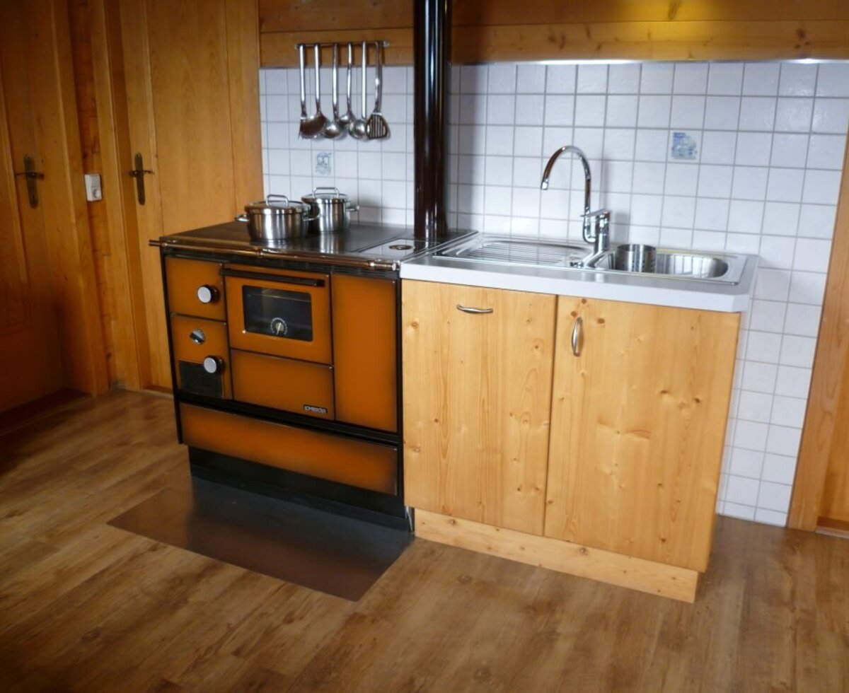 The fully equipped kitchen in the Alpine hut includes a wood-burning stove with an oven, a sink, and cooking utensils.