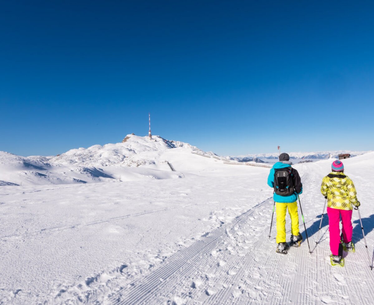 Two people snowshoeing on a groomed winter path in the snowy mountains, an activity available near the Farm House.
