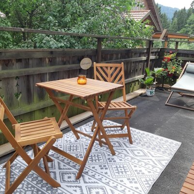 The Farm House features an outdoor patio with a wooden table, two chairs, and a lounge chair, set against a backdrop of natural greenery.