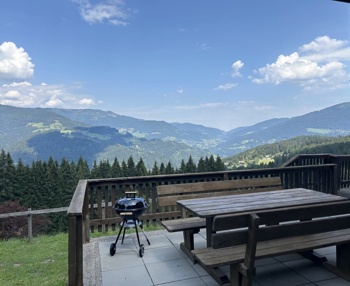 The Almhaus's inviting terrace features rustic wooden seating, a barbecue grill, and expansive views of the lush mountains.