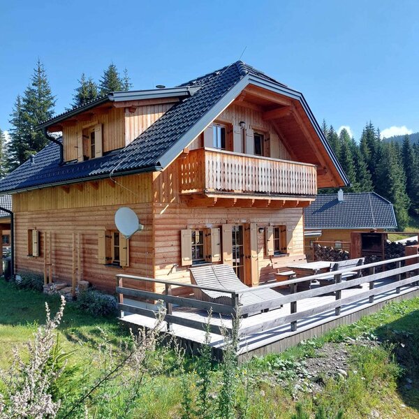 An inviting Alm featuring a spacious wooden terrace with a sun lounger, a balcony, and tranquil forest surroundings.