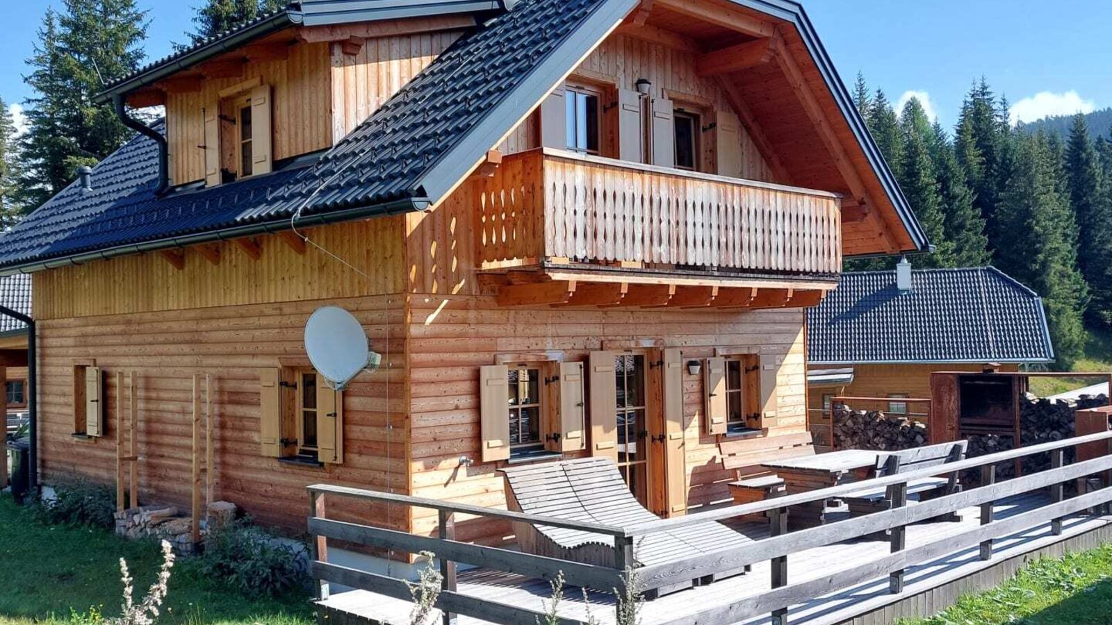 An inviting Alm featuring a spacious wooden terrace with a sun lounger, a balcony, and tranquil forest surroundings.