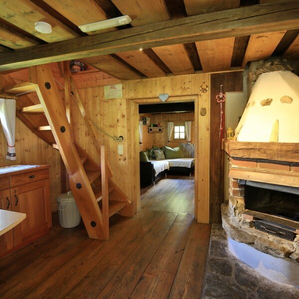 The Alpine Hut's open-plan living area features a wood-fired stove, a wooden staircase leading to the upper floor, and an adjacent kitchen counter. The Alpine Hut's open-plan living area features a wood-fired stove, a wooden staircase leading to the upper floor, and an adjacent kitchen counter.