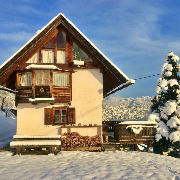 The snow-covered Alpine Hut features stacked firewood and is set against a winter landscape with an evergreen tree and distant mountains. The snow-covered Alpine Hut features stacked firewood and is set against a winter landscape with an evergreen tree and distant mountains.