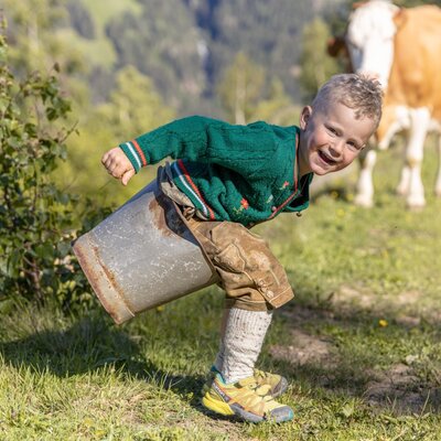A young boy playing on the grassy hillside near the Alpine Hut, with a cow grazing in the background.
