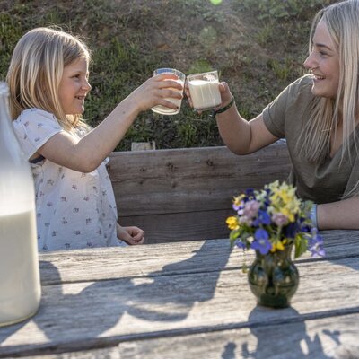 Guests enjoying fresh milk at an outdoor wooden table at the Alpine Hut.