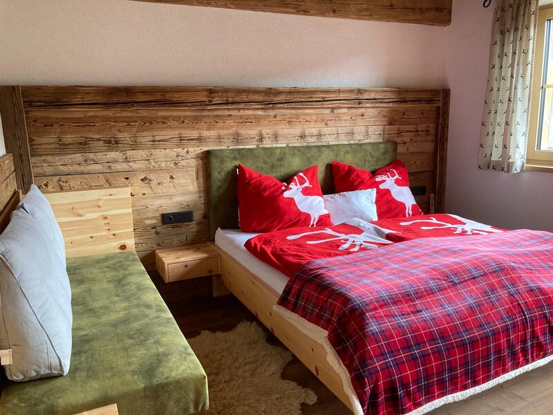 Bedroom in the Alm featuring a double bed, wooden wall paneling, and a green upholstered bench.
