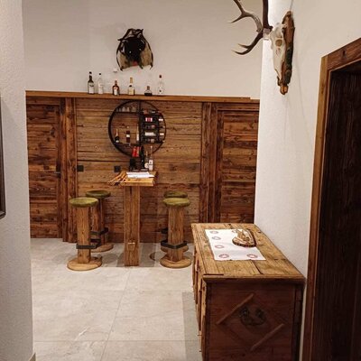 The bar area of the Alm, featuring wooden elements, bar stools, and a selection of drinks, decorated with a deer skull.