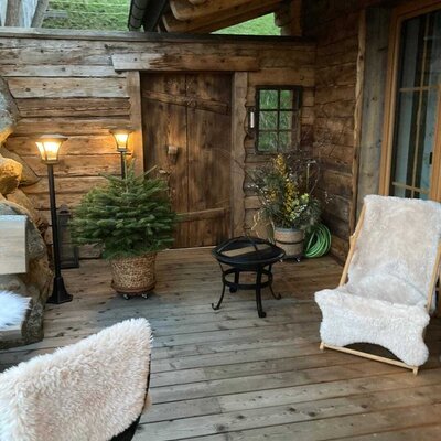 The Alm's wooden terrace features two chairs with sheepskin throws, two outdoor lamps, and a fire pit.