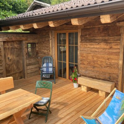 The wooden terrace of the Alm, featuring a dining table, various seating options, and a deck chair.