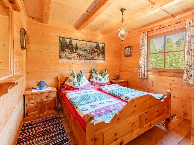 Double bedroom in the Alm with solid Swiss pine furniture, two bedside tables, a mirror console, and a window view of greenery.