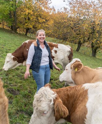 A woman among cows in the pasture surrounding the Alpine Hut, with autumn trees in the background.