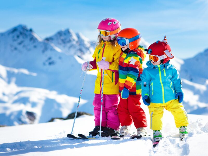 Three children in ski gear on a snowy mountain, demonstrating the farm house's suitability for family ski holidays, supported by its ski cellar.