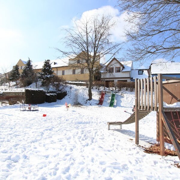 The Farm House offers an outdoor children's playground with a wooden climbing structure, slides, swings, and a seesaw, set in a snowy area.