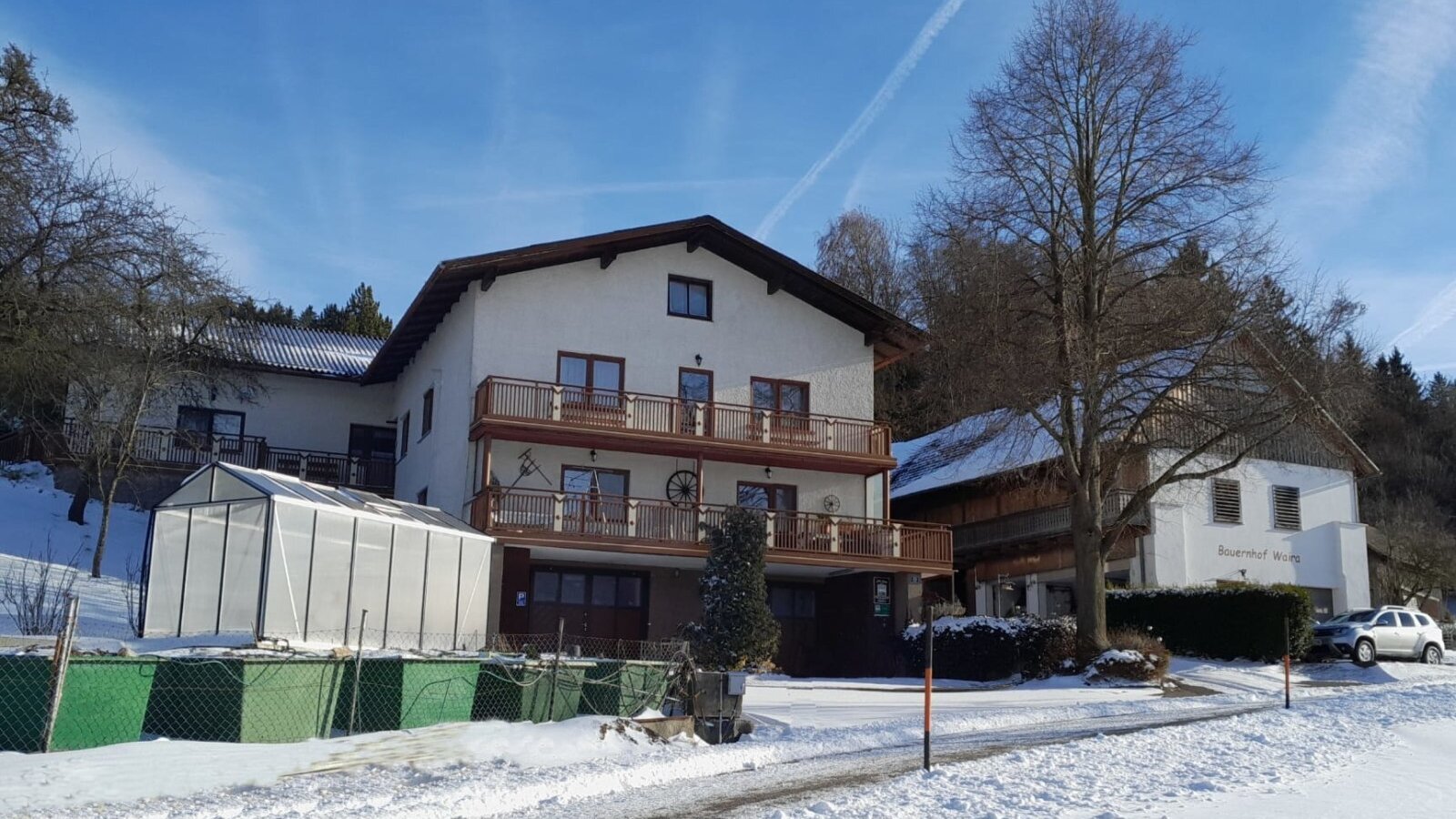 Exterior view of the farmhouse in winter, featuring balconies and a greenhouse.