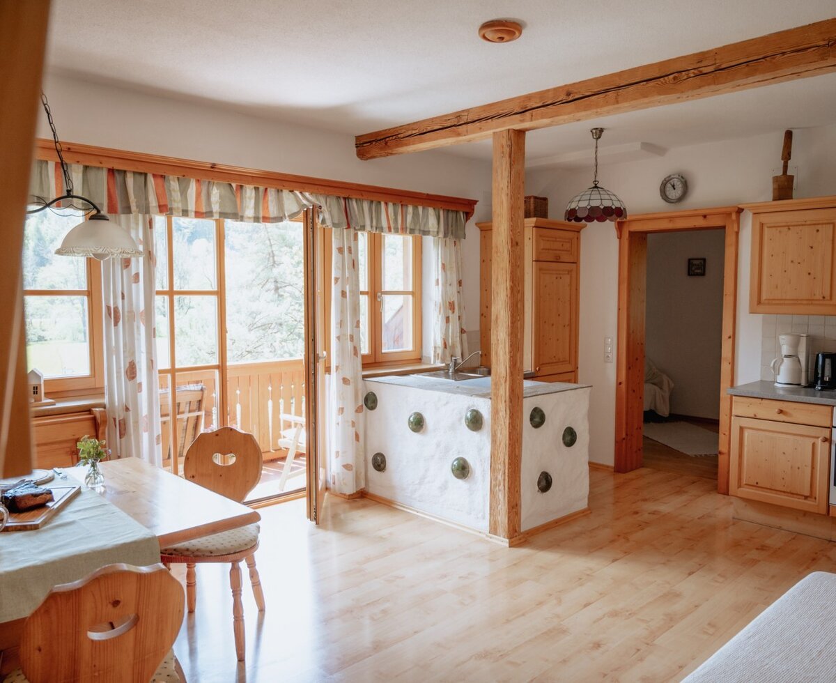 The kitchen and dining area of the Farm House offers a wooden table, kitchen appliances, and direct access to a balcony.