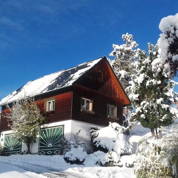 The Farm House exterior in winter, with its wooden and white facade, surrounded by snow-covered trees under a clear blue sky.
